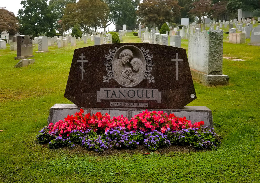 A grave with flowers and a tombstone in the background.